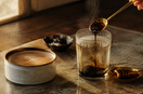 Editorial morning ritual of shilajit resin dissolving into warm water beside coffee and honey